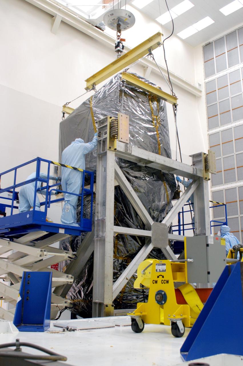 KENNEDY SPACE CENTER, FLA. - Inside Hangar AE at Cape Canaveral Air Force Station (CCAFS), workers secure the Swift spacecraft, wrapped in a protective cover, on a work stand. Swift is a first-of-its-kind, multi-wavelength observatory dedicated to the study of gamma-ray burst (GRB) science. Its three instruments will work together to observe GRBs and afterglows in the gamma-ray, X-ray and optical wavebands. Swift is part of NASA’s medium explorer (MIDEX) program being developed by an international collaboration. It will be launched no earlier than Oct. 7 into a low-Earth orbit on a Boeing Delta 7320 rocket from pad 17-A at CCAFS. During its nominal 2-year mission, Swift is expected to observe more than 200 bursts, which will represent the most comprehensive study of GRB afterglow to date.