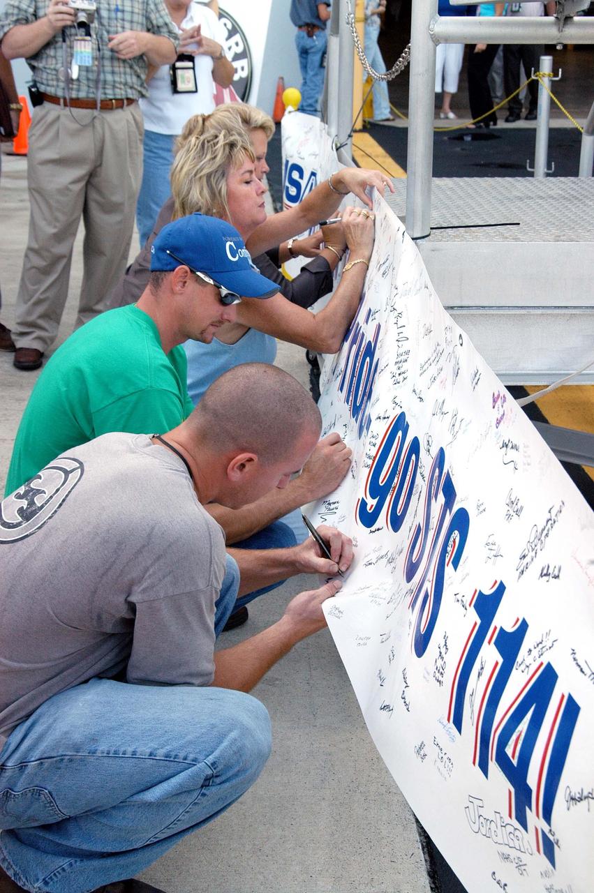 KENNEDY SPACE CENTER, FLA. - Employees in the Assembly and Refurbishment Facility sign a banner recognizing their efforts in preparing the first (left) solid rocket booster aft skirt for mission STS-114 on schedule.  The segment will be transferred to the Rotation Processing and Surge Facility (RPSF) for stacking.  At the RPSF an aft motor segment and an external tank attach ring will be installed.  The stack will then be moved to the Vehicle Assembly Building for further build-up. This is the first transfer of a large piece of hardware from SRB to Ground Operations.  It is a significant milestone in the march to Return to Flight.