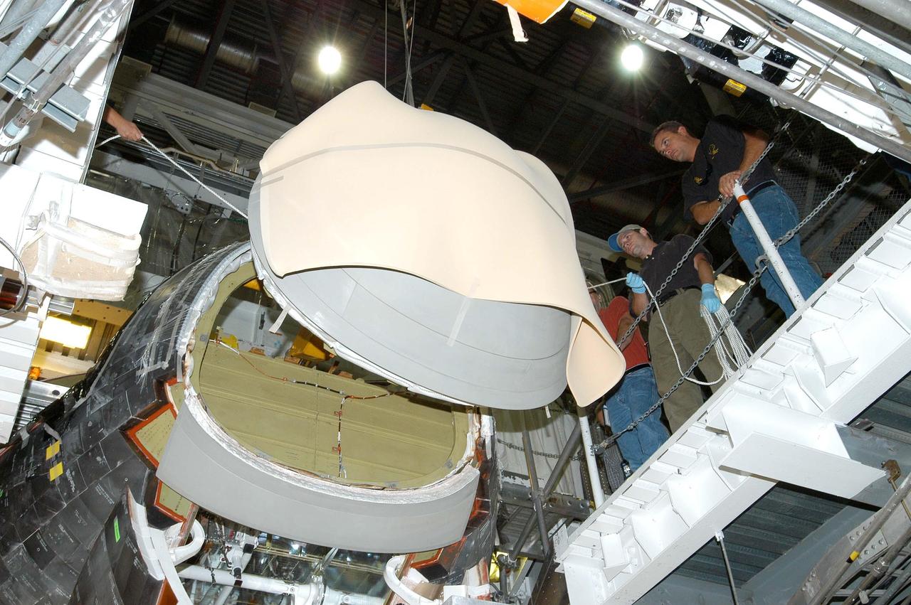 KENNEDY SPACE CENTER, FLA. - In the Orbiter Processing Facility, workers help install the nose cap on the orbiter Atlantis. The nose cap was removed from the vehicle in May and sent back to the vendor for thorough Non-Destructive Engineering evaluation and recoating.  Thermography was also performed to check for internal flaws.  This procedure uses high intensity light to heat areas that are immediately scanned with an infrared camera.  White Thermal Protection System blankets were reinstalled on the nose cap before installation.  Processing continues on Atlantis for its future mission to the International Space Station.