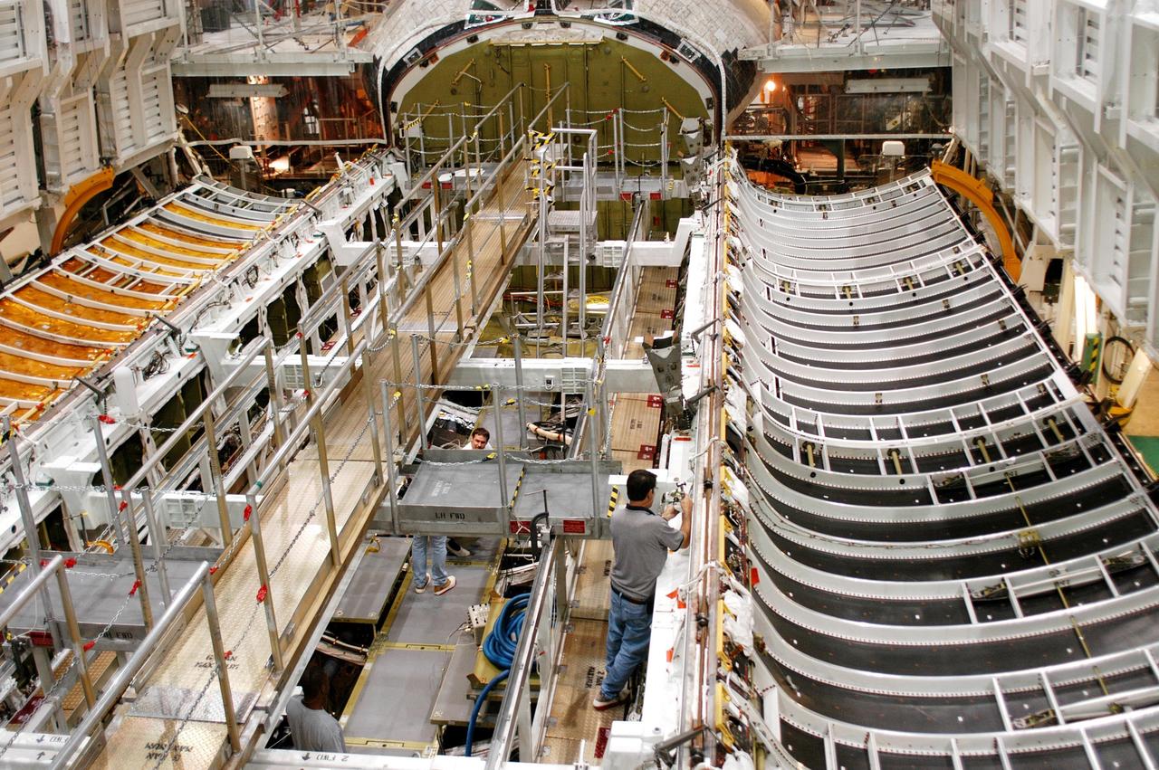 KENNEDY SPACE CENTER, FLA. -  In the Orbiter Processing Facility, workers prepare to close the payload bay doors on Atlantis in preparation for the expected impact of Hurricane Frances on Saturday. Other preparations at KSC include powering down the Space Shuttle orbiters and stowing the landing gear.  Workers are also taking precautions against flooding by moving spacecraft hardware off the ground and sandbagging facilities. The Orbiter Processing Facility is constructed of concrete and steel and was designed to withstand winds of 105 mph.  The Vehicle Assembly Building is constructed of concrete and steel and was designed to withstand winds of 125 mph. Other payload and flight hardware support facilities can endure winds of 110 mph.  Launch pads and the Payload Hazardous Servicing Facility can withstand 125-mph winds.