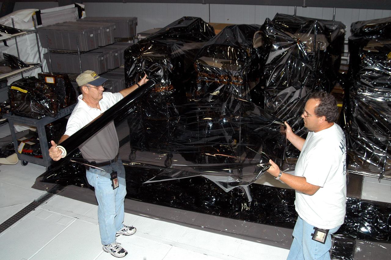 KENNEDY SPACE CENTER, FLA. -  Workers in the Orbiter Processing Facility unwrap plastic for use in covering equipment as part of preparations for the expected impact of Hurricane Frances on Saturday. Other preparations at KSC include powering down the Space Shuttle orbiters, closing the payload bay doors and stowing the landing gear.  Workers are also taking precautions against flooding by moving spacecraft hardware off the ground and sandbagging facilities. The Orbiter Processing Facility is constructed of concrete and steel and was designed to withstand winds of 105 mph.  The Vehicle Assembly Building is constructed of concrete and steel and was designed to withstand winds of 125 mph. Other payload and flight hardware support facilities can endure winds of 110 mph.  Launch pads and the Payload Hazardous Servicing Facility can withstand 125-mph winds.