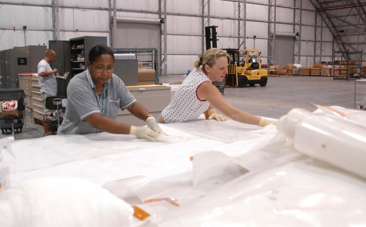 KENNEDY SPACE CENTER, FLA. -  In the RLV hangar at KSC, United Space Alliance workers Beth Smith (left) and Theresa Haygood unwrap equipment removed from the hurricane-ravaged Thermal Protection System Facility (TPSF).  The facility, which creates the TPS tiles, blankets and all the internal thermal control systems for the Space Shuttles, is almost totally unserviceable at this time after losing approximately 35 percent of its roof due to Hurricane Frances, which blew across Central Florida Sept. 4-5.  The maximum wind at the surface from Hurricane Frances was 94 mph from the northeast at 6:40 a.m. on Sunday, September 5.  It was recorded at a weather tower located on the east shore of the Mosquito Lagoon near the Cape Canaveral National Seashore.  The highest sustained wind at KSC was 68 mph.