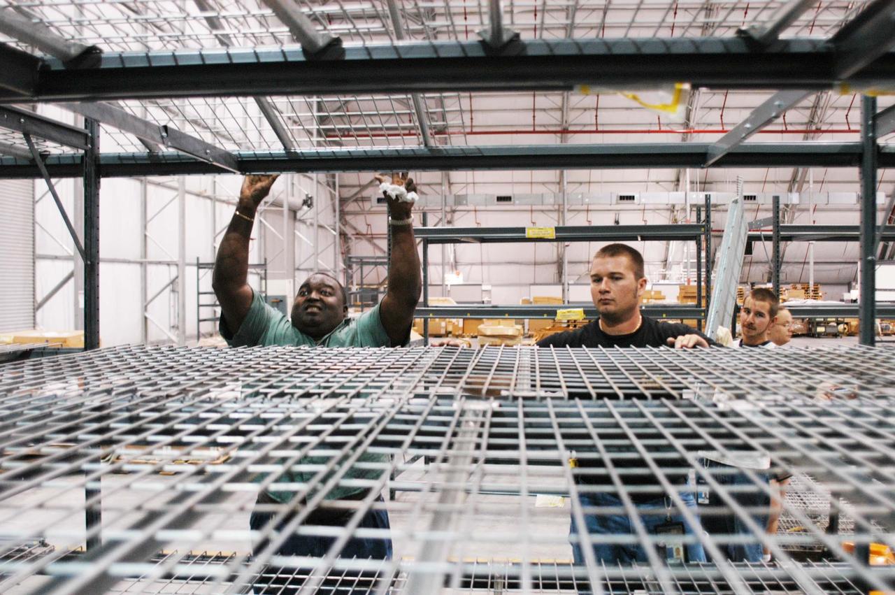 KENNEDY SPACE CENTER, FLA. -  In the RLV hangar at KSC, United Space Alliance workers Matt Carter (left) and Mike Sherman set up racks to hold equipment removed from the hurricane-ravaged Thermal Protection System Facility (TPSF).  The facility, which creates the TPS tiles, blankets and all the internal thermal control systems for the Space Shuttles, is almost totally unserviceable at this time after losing approximately 35 percent of its roof due to Hurricane Frances, which blew across Central Florida Sept. 4-5.  The maximum wind at the surface from Hurricane Frances was 94 mph from the northeast at 6:40 a.m. on Sunday, September 5.  It was recorded at a weather tower located on the east shore of the Mosquito Lagoon near the Cape Canaveral National Seashore.  The highest sustained wind at KSC was 68 mph.
