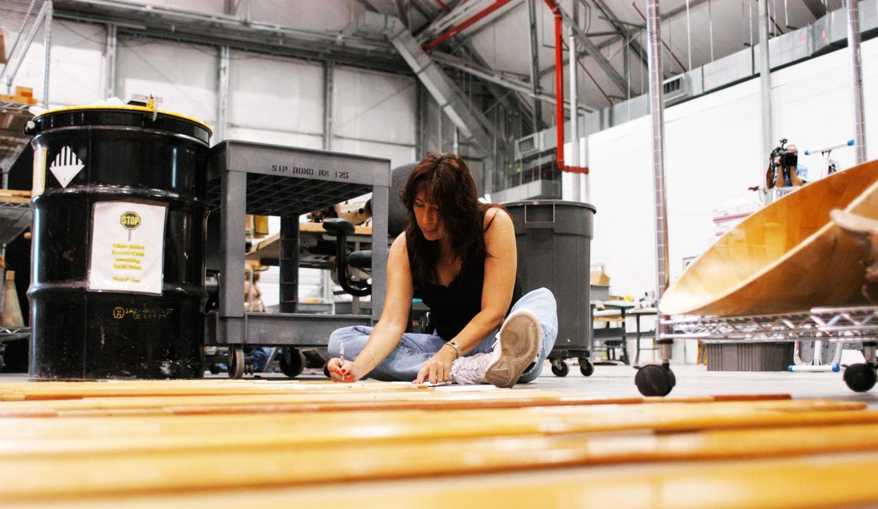KENNEDY SPACE CENTER, FLA. -  United Space Alliance worker  Kathy Evans works on equipment in the temporary tile shop set up in the RLV hangar at KSC.  The hurricane-ravaged Thermal Protection System Facility (TPSF), which creates the TPS tiles, blankets and all the internal thermal control systems for the Space Shuttles, is almost totally unserviceable at this time after losing approximately 35 percent of its roof due to Hurricane Frances, which blew across Central Florida Sept. 4-5.  Undamaged equipment was removed from the TPSF and stored in the hangar.  The maximum wind at the surface from Hurricane Frances was 94 mph from the northeast at 6:40 a.m. on Sunday, September 5.  It was recorded at a weather tower located on the east shore of the Mosquito Lagoon near the Cape Canaveral National Seashore.  The highest sustained wind at KSC was 68 mph.