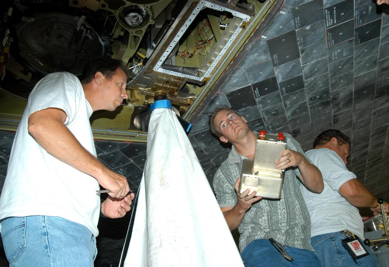 KENNEDY SPACE CENTER, FLA. - In the Orbiter Processing Facility, from left, United Space Alliance workers Loyd Turner, Craig Meyer and Erik Visser prepare to conduct a fit check of an External Tank (ET) digital still camera in the right-hand liquid oxygen umbilical well on Space Shuttle Atlantis. NASA is pursuing use of the camera, beginning with the Shuttle’s Return To Flight, to obtain and downlink high-resolution images of the ET following separation of the ET from the orbiter after launch. The Kodak camera will record 24 images, at one frame per 1.5 seconds, on a flash memory card. After orbital insertion, the crew will transfer the images from the memory card to a laptop computer. The files will then be downloaded through the Ku-band system to the Mission Control Center in Houston for analysis.
