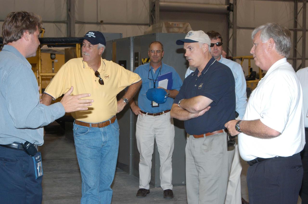 KENNEDY SPACE CENTER, FLA. -  From left, Martin Wilson, manager of Thermal Protection System (TPS) operations for United Space Alliance, briefs NASA Administrator Sean O’Keefe, KSC Director of the Spaceport Services Scott Kerr, NASA Associate Administrator of the Space Operations Mission Directorate William Readdy, and Center Director James Kennedy (right) on the temporary tile shop set up in the RLV hangar.  O’Keefe and Readdy are visiting KSC to survey the damage sustained by KSC facilities from Hurricane Frances. The Thermal Protection System Facility (TPSF), which creates the TPS tiles, blankets and all the internal thermal control systems for the Space Shuttles, is almost totally unserviceable at this time after losing approximately 35 percent of its roof in the storm, which blew across Central Florida Sept. 4-5. Undamaged equipment was removed from the TPSF and stored in the hangar. NASA’s three Space Shuttle orbiters -- Discovery, Atlantis and Endeavour - along with the Shuttle launch pads, all of the critical flight hardware for the orbiters and the International Space Station, and NASA’s Swift spacecraft, awaiting launch in October, were well protected and unharmed.