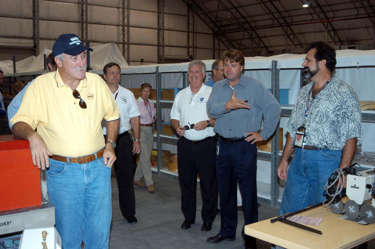 KENNEDY SPACE CENTER, FLA. -  Martin Wilson (second from right), manager of Thermal Protection System (TPS) operations for United Space Alliance (USA) , introduces Kevin Harrington, manager of Soft Goods Production in the TPSF, during a briefing to (from left) NASA Administrator Sean O’Keefe, KSC Director of Shuttle Processing Michael E. Wetmore, Center Director James Kennedy and KSC Director of the Spaceport Services Scott Kerr (behind Kennedy), on the temporary tile shop set up in the RLV hangar.  O’Keefe and NASA Associate Administrator of  Space Operations Mission Directorate William Readdy are visiting KSC to survey the damage sustained by KSC facilities from Hurricane Frances. The Thermal Protection System Facility (TPSF), which creates the TPS tiles, blankets and all the internal thermal control systems for the Space Shuttles, is almost totally unserviceable at this time after losing approximately 35 percent of its roof in the storm, which blew across Central Florida Sept. 4-5. The Labor Day storm also caused significant damage to the Vehicle Assembly Building and Processing Control Center.  Additionally, the Operations and Checkout Building, Vertical Processing Facility, Hangar AE, Hangar S and Hangar AF Small Parts Facility each received substantial damage. Undamaged equipment was removed from the TPSF and stored in the hangar. However, well-protected and unharmed were NASA’s three Space Shuttle orbiters -- Discovery, Atlantis and Endeavour - along with the Shuttle launch pads, all of the critical flight hardware for the orbiters and the International Space Station, and NASA’s Swift spacecraft that is awaiting launch in October.