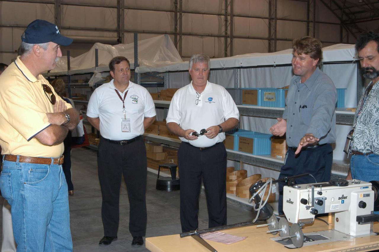 KENNEDY SPACE CENTER, FLA. -  Martin Wilson (second from right), manager of Thermal Protection System (TPS) operations for United Space Alliance (USA), briefs NASA Administrator Sean O’Keefe, KSC Director of Shuttle Processing Michael E. Wetmore and Center Director James Kennedy about the temporary tile shop set up in the RLV hangar.  At far right is USA Manager of Soft Goods Production in the TPSF, Kevin Harrington. O’Keefe and NASA Associate Administrator of  Space Operations Mission Directorate William Readdy are visiting KSC to survey the damage sustained by KSC facilities from Hurricane Frances. The Thermal Protection System Facility (TPSF), which creates the TPS tiles, blankets and all the internal thermal control systems for the Space Shuttles, is almost totally unserviceable at this time after losing approximately 35 percent of its roof in the storm, which blew across Central Florida Sept. 4-5. Undamaged equipment was removed from the TPSF and stored in the hangar. The Labor Day storm also caused significant damage to the Vehicle Assembly Building and Processing Control Center.  Additionally, the Operations and Checkout Building, Vertical Processing Facility, Hangar AE, Hangar S and Hangar AF Small Parts Facility each received substantial damage. However, well-protected and unharmed were NASA’s three Space Shuttle orbiters -- Discovery, Atlantis and Endeavour - along with the Shuttle launch pads, all of the critical flight hardware for the orbiters and the International Space Station, and NASA’s Swift spacecraft that is awaiting launch in October.