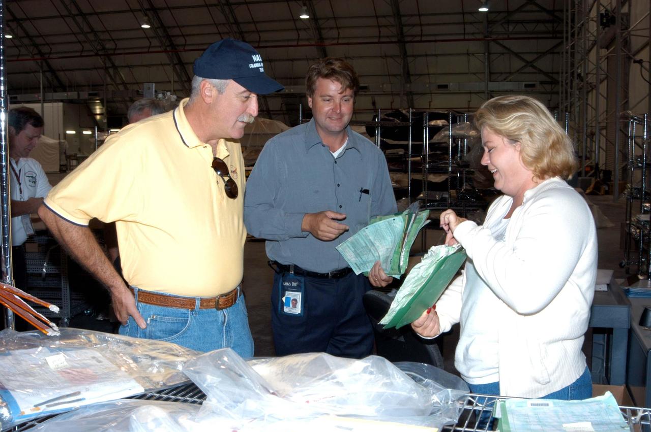 KENNEDY SPACE CENTER, FLA. -  -  United Space Alliance technician Shelly Kipp (right) shows some of the material salvaged from the storm-ravaged Thermal Protection System Facility (TPSF) to NASA Administrator Sean O’Keefe (left).  Martin Wilson (center), manager of TPS operations for USA, looks on.  The TPSF, which creates the TPS tiles, blankets and all the internal thermal control systems for the Space Shuttles, is almost totally unserviceable at this time after losing approximately 35 percent of its roof during Hurricane Frances, which blew across Central Florida Sept. 4-5. O’Keefe and NASA Associate Administrator of  Space Operations Mission Directorate William Readdy are visiting KSC to survey the damage sustained by KSC facilities from the hurricane.  Undamaged equipment was removed from the TPSF and stored in the RLV hangar. The Labor Day storm also caused significant damage to the Vehicle Assembly Building and Processing Control Center.  Additionally, the Operations and Checkout Building, Vertical Processing Facility, Hangar AE, Hangar S and Hangar AF Small Parts Facility each received substantial damage. However, well-protected and unharmed were NASA’s three Space Shuttle orbiters -- Discovery, Atlantis and Endeavour - along with the Shuttle launch pads, all of the critical flight hardware for the orbiters and the International Space Station, and NASA’s Swift spacecraft that is awaiting launch in October.