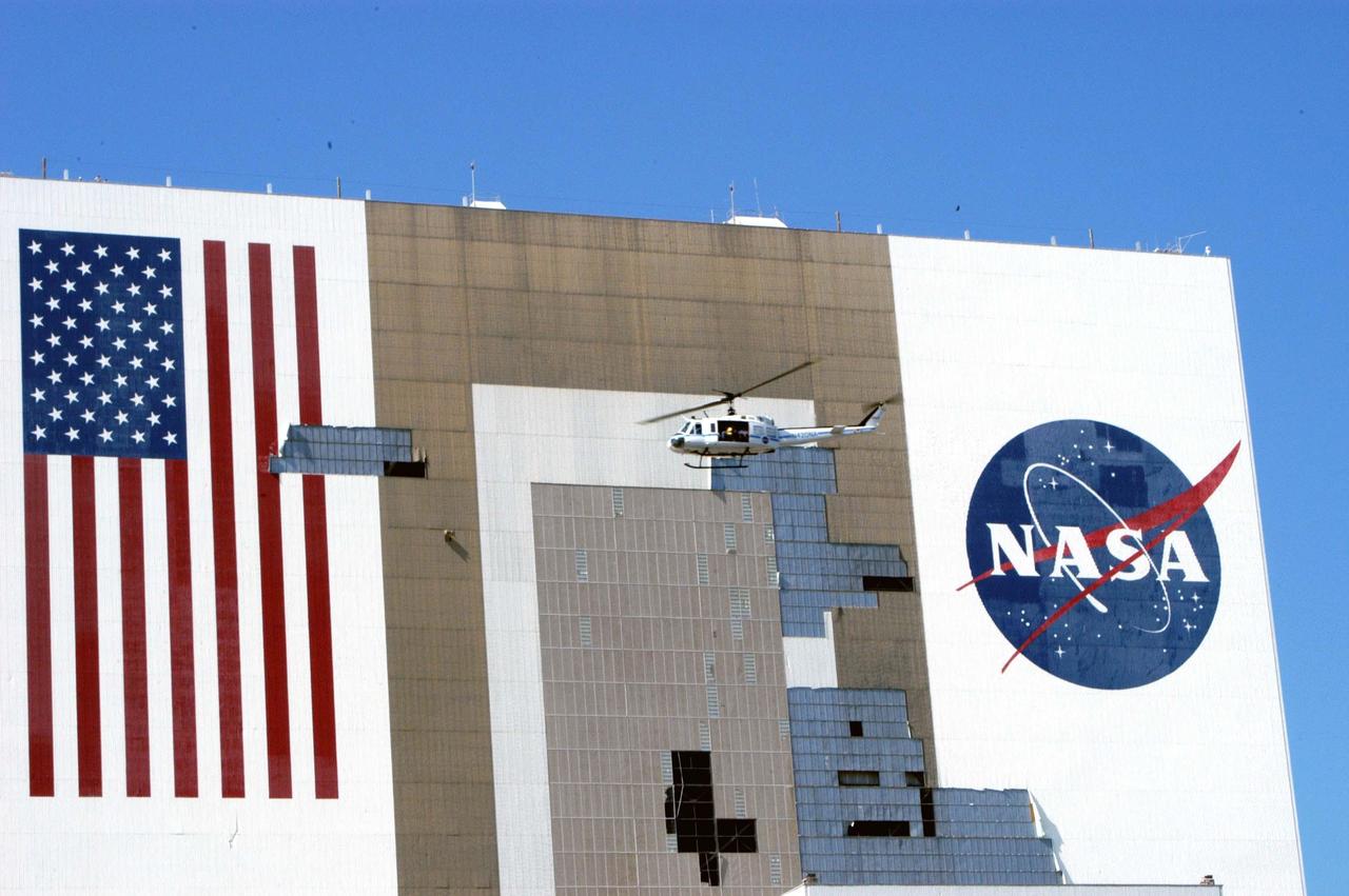 KENNEDY SPACE CENTER, FLA. -  The helicopter carrying NASA Administrator Sean O’Keefe and KSC Director of Spaceport Services Scott Kerr passes by the Vehicle Assembly Building (VAB) to observe the damage inflicted by Hurricane Frances over the Labor Day weekend.  The VAB lost approximately 850 tiles on the south wall, seen here.  O’Keefe and NASA Associate Administrator of  Space Operations Mission Directorate William Readdy are visiting KSC to survey the damage sustained by KSC facilities from the hurricane.  The storm also caused significant damage to the Thermal Protection System Facility and Processing Control Center.  Additionally, the Operations and Checkout Building, Vertical Processing Facility, Hangar AE, Hangar S and Hangar AF Small Parts Facility each received substantial damage. However, well-protected and unharmed were NASA’s three Space Shuttle orbiters -- Discovery, Atlantis and Endeavour - along with the Shuttle launch pads, all of the critical flight hardware for the orbiters and the International Space Station, and NASA’s Swift spacecraft that is awaiting launch in October.
