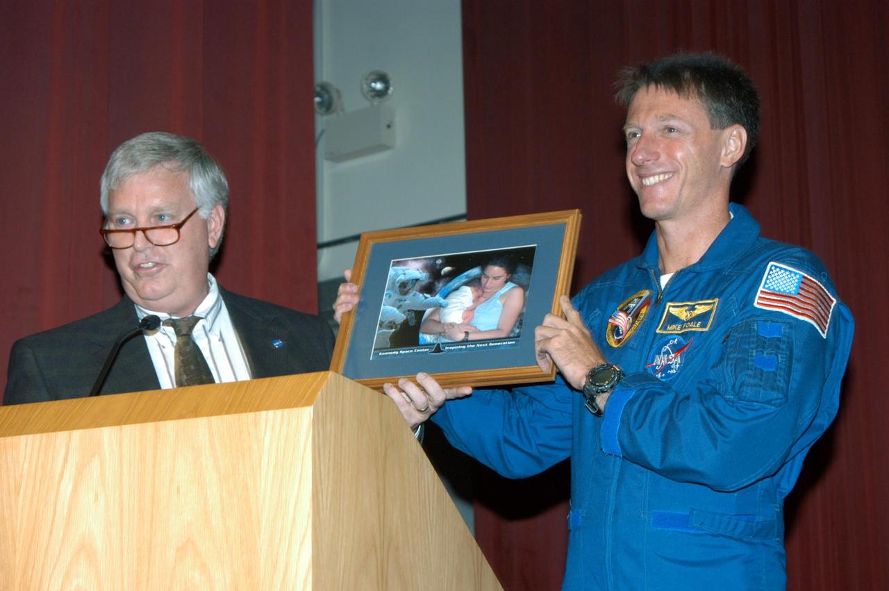 KENNEDY SPACE CENTER, FLA. -  In the Training Auditorium, Center Director Jim Kennedy presents a framed photo to astronaut Mike Foale, who spoke to the audience about his experiences aboard the International Space Station as commander of the Expedition 8 crew.  Foale and Flight Engineer Alexander Kaleri spent 194 days, 18 hours and 35 minutes in space, the second longest expedition to be completed aboard the Station. In February Foale and Kaleri conducted the first spacewalk ever performed from the complex by a two-person crew.   Foale has accumulated more time in space than any U.S. astronaut, amassing a total of 374 days, 11 hours and 19 minutes in space from his Expedition 8 mission, a 1997 flight to the Russian Mir Space Station, and four Space Shuttle missions.