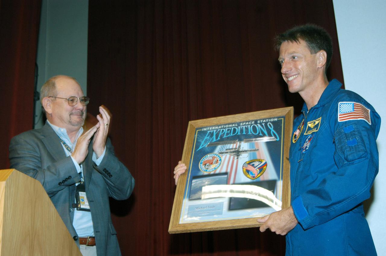KENNEDY SPACE CENTER, FLA. -  In the Training Auditorium, James Hattaway Jr., KSC associate director, presents a framed graphic to astronaut Mike Foale representing his stay aboard  the International Space Station as commander of the Expedition 8 crew. .Foale spoke to the audience of employees about his experiences aboard the Space Station.  Foale and Flight Engineer Alexander Kaleri spent 194 days, 18 hours and 35 minutes in space, the second longest expedition to be completed aboard the Station. In February Foale and Kaleri conducted the first spacewalk ever performed from the complex by a two-person crew.   Foale has accumulated more time in space than any U.S. astronaut, amassing a total of 374 days, 11 hours and 19 minutes in space from his Expedition 8 mission, a 1997 flight to the Russian Mir Space Station, and four Space Shuttle missions.