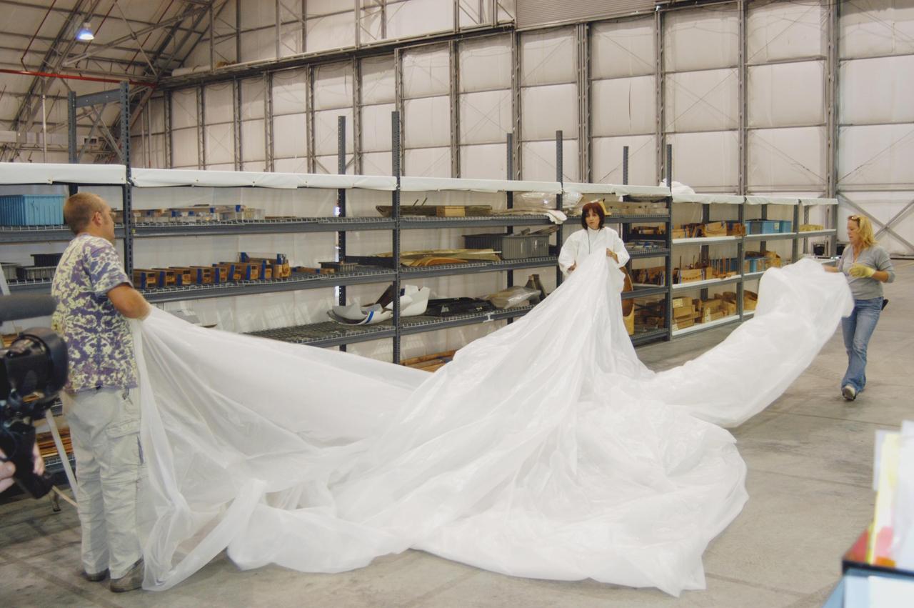 KENNEDY SPACE CENTER, FLA. - In preparation for the arrival of Hurricane Jeanne, workers in the Reusable Launch Vehicle Hangar unroll long pieces of plastic to place on shelves holding Thermal Protection System Facility (TPSF) equipment.  Jeanne is expected to impact Central Florida Sunday. This is the fourth hurricane in 45 days to make landfall somewhere in the state.  The TPSF suffered extensive damage from Hurricane Frances, causing the relocation of equipment and materials to the hangar.