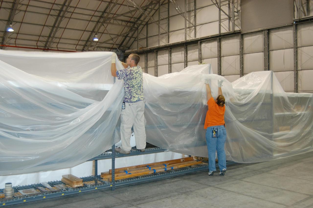 KENNEDY SPACE CENTER, FLA. - In the Reusable Launch Vehicle (RLV) Hangar, workers secure stretch sheets of plastic over racks of equipment in preparation for the arrival of Hurricane Jeanne, expected to impact Central Florida Sunday. This is the fourth hurricane in 45 days to make landfall somewhere in the state.  The Thermal Protection System (TPS) Facility suffered extensive damage from Hurricane Frances, causing the relocation of equipment to the RLV.