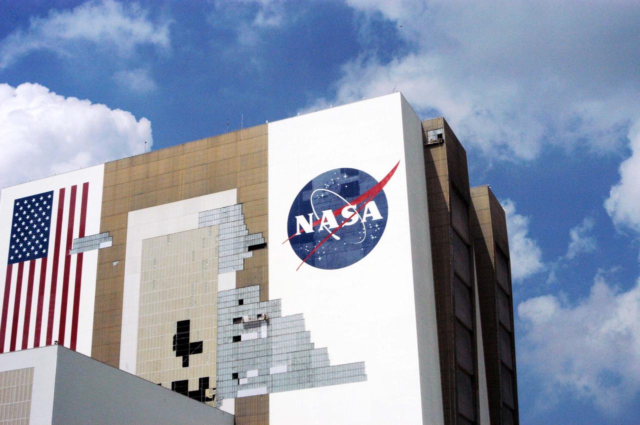 KENNEDY SPACE CENTER, FLA. - On a scaffold barely visible along the south wall of the Vehicle Assembly Building near the NASA logo, workers are covering the holes with corrugated steel so the facility can be returned to performing operational activities. The VAB lost 820 panels from the south wall during the storm, and 25 additional panels pulled off the east wall by Hurricane Jeanne. Another scaffold is suspended near the top of the east wall (right side) for repairs. The VAB stands 525 feet tall. Central Florida, including Kennedy Space Center, has been battered by four hurricanes between Aug. 13 and Sept. 26.