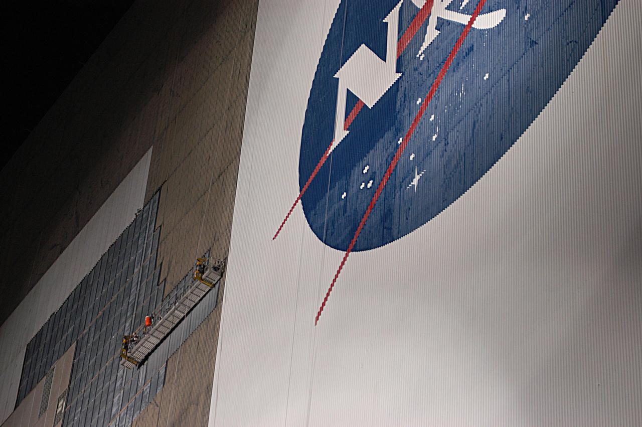KENNEDY SPACE CENTER, FLA. - The south wall of the Vehicle Assembly Building is bathed in light at night to allow workers on a scaffold (at left) to cover the holes with corrugated steel so the facility can be returned to performing operational activities. Xenon lights on the ground provide the illumination. The VAB lost 820 panels from the south wall during Frances, and 25 additional panels during Hurricane Jeanne. The VAB stands 525 feet tall. Central Florida, including Kennedy Space Center, was battered by four hurricanes between Aug. 13 and Sept. 26.