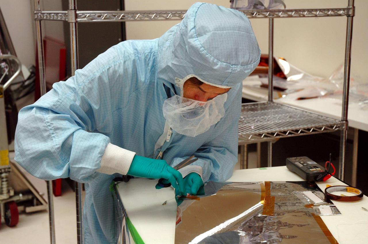 KENNEDY SPACE CENTER, FLA. - Hangar AE, Cape Canaveral Air Force Station, a technician trims blanket material that will be installed around the Swift spacecraft.  The blankets provide thermal stability during the mission.  Swift is a first-of-its-kind multi-wavelength observatory dedicated to the study of gamma-ray burst (GRB) science. Its three instruments will work together to observe GRBs and afterglows in the gamma ray, X-ray, ultraviolet and optical wavebands. Swift is expected to observe more than 200 gamma-ray bursts - the most comprehensive study of GRB afterglows to date - during its 2-year mission.