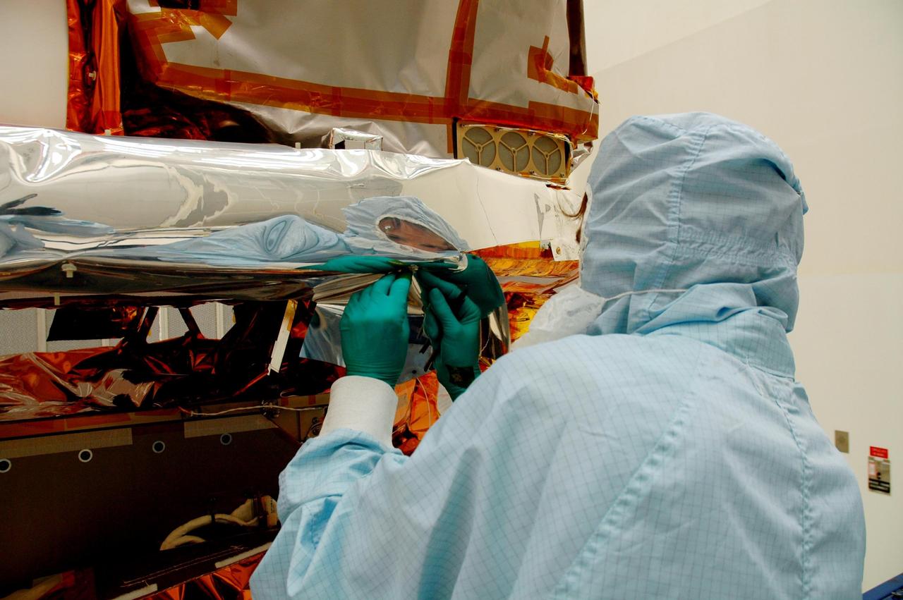 KENNEDY SPACE CENTER, FLA. - At Hangar AE, Cape Canaveral Air Force Station, a technician (right) watches while another completes installation of the blankets around the Swift spacecraft.  The blankets provide thermal stability during the mission.  Swift is a first-of-its-kind multi-wavelength observatory dedicated to the study of gamma-ray burst (GRB) science. Its three instruments will work together to observe GRBs and afterglows in the gamma ray, X-ray, ultraviolet and optical wavebands. Swift is expected to observe more than 200 gamma-ray bursts - the most comprehensive study of GRB afterglows to date - during its 2-year mission.