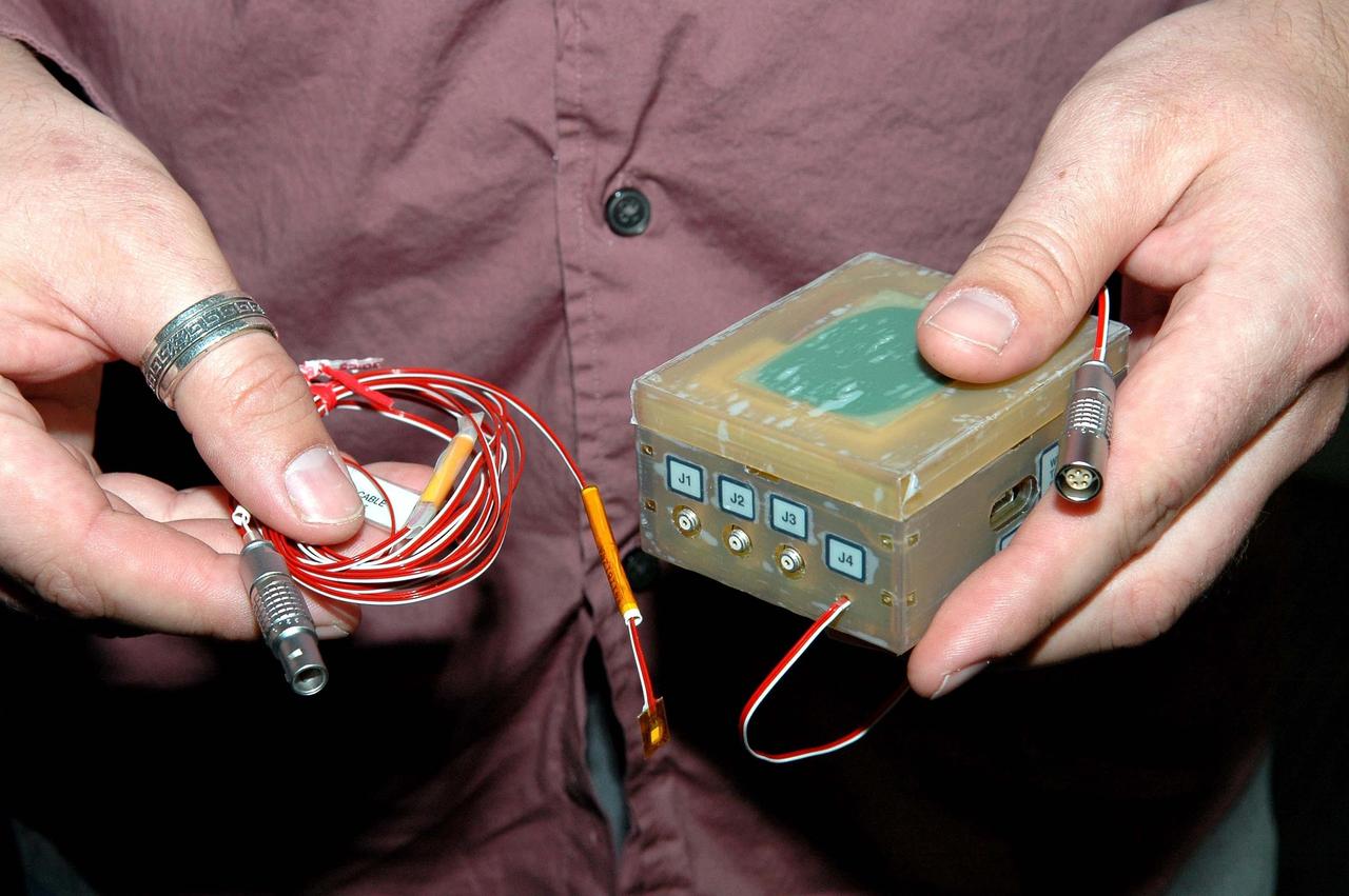 KENNEDY SPACE CENTER, FLA.  - During an installation demonstration the Orbiter Processing Facility, Robert Early, lead instrument engineer with United Space Alliance, holds components of the sensor system being placed on the wing leading edge of orbiter Discovery.  The sensors are part of the Wing Leading Edge Impact Detection System, a new safety measure added for all future Space Shuttle missions. The system also includes accelerometers that monitor the orbiter's wings for debris impacts during launch and while in orbit. There are 22 temperature sensors and 66 accelerometers on each wing. Sensor data will flow from the wing to the crew compartment, where it will be transmitted to Earth.