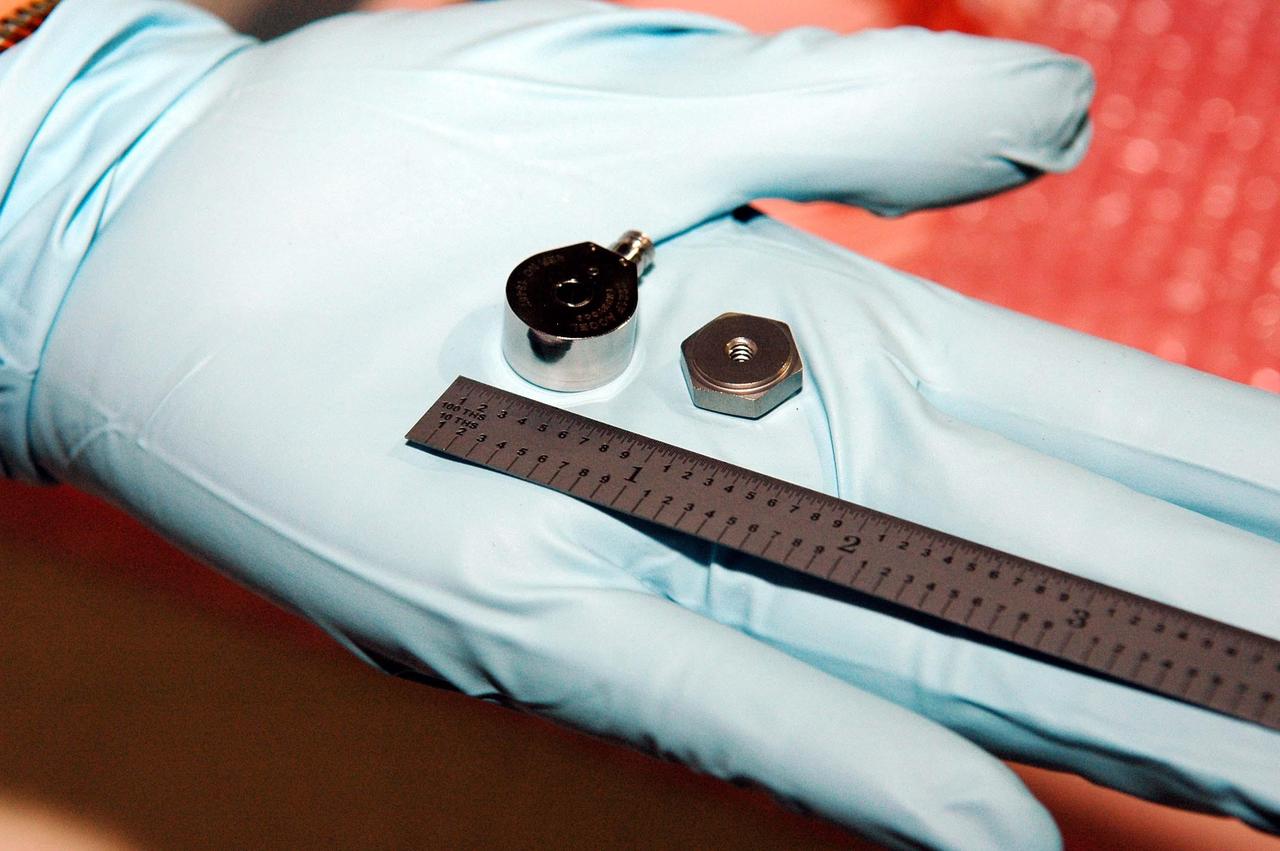 KENNEDY SPACE CENTER, FLA. - This photo shows the size of the sensors being placed on the wing leading edge of orbiter Discovery. In her hand, United Space Alliance technician Lisa Campbell holds an accelerometer (left), which will eventually be installed on a mounting nut. The sensors are part of the Wing Leading Edge Impact Detection System, a new safety measure added for all future Space Shuttle missions. The system also includes accelerometers that monitor the orbiter's wings for debris impacts during launch and while in orbit. There are 22 temperature sensors and 66 accelerometers on each wing. Sensor data will flow from the wing to the crew compartment, where it will be transmitted to Earth.