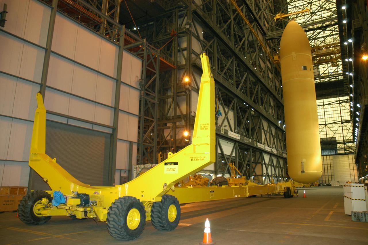 KENNEDY SPACE CENTER, FLA. - After being lowered from its cell in the Vehicle Assembly Building,  External Tank 118 (ET-118) is suspended above the transfer aisle before being placed on the transporter at left.  The tank will be transferred to NASA’s Michoud Assembly Facility in New Orleans.  The tank is being installed with an improved bipod fitting, which connects the external fuel tank to the Shuttle during launch. The new design, a significant milestone in the effort to return the Shuttle to safe flight, replaces the foam that was used to prevent ice buildup on the tank’s bipod fittings with four rod-shaped heaters.  The heaters are being retrofitted on the 11 existing tanks and incorporated into the manufacture of all new tanks.