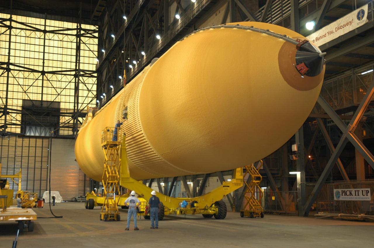 KENNEDY SPACE CENTER, FLA. - Workers in the transfer aisle of the Vehicle Assembly Building check the progress of External Tank 118 (ET-118) as it is lowered onto the transporter below it.  The tank will be transferred to NASA’s Michoud Assembly Facility in New Orleans. The tank is being installed with an improved bipod fitting, which connects the external fuel tank to the Shuttle during launch. The new design, a significant milestone in the effort to return the Shuttle to safe flight, replaces the foam that was used to prevent ice buildup on the tank’s bipod fittings with four rod-shaped heaters.  The heaters are being retrofitted on the 11 existing tanks and incorporated into the manufacture of all new tanks.