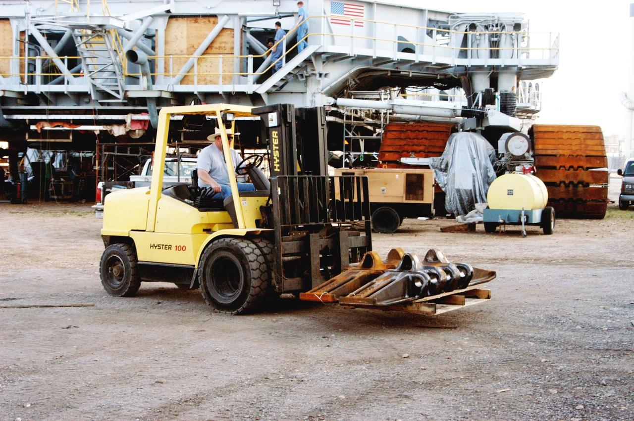 KENNEDY SPACE CENTER, FLA. - In the Crawler Transporter (CT) area, a worker offloads some of the new crawler shoes that arrived. In the background is one of the two CTs. The new shoes were manufactured by ME Global in Duluth, Minn. The CT transports the Mobile Launcher Platform, with the assembled Space Shuttle aboard, between the refurbishment area, the VAB and Launch Complex Pads 39A and 39B. The crawlers have 456 shoes, 57 per belt (8 belts in all). Each shoe weighs 2,200 pounds. The original shoes were manufactured for the Apollo Program. Cracks appeared in the shoes in recent years spurring a need for replacement. The new manufacturer, in Duluth, Minn., has improved the design for Return to Flight and use through the balance of the Space Shuttle Program.