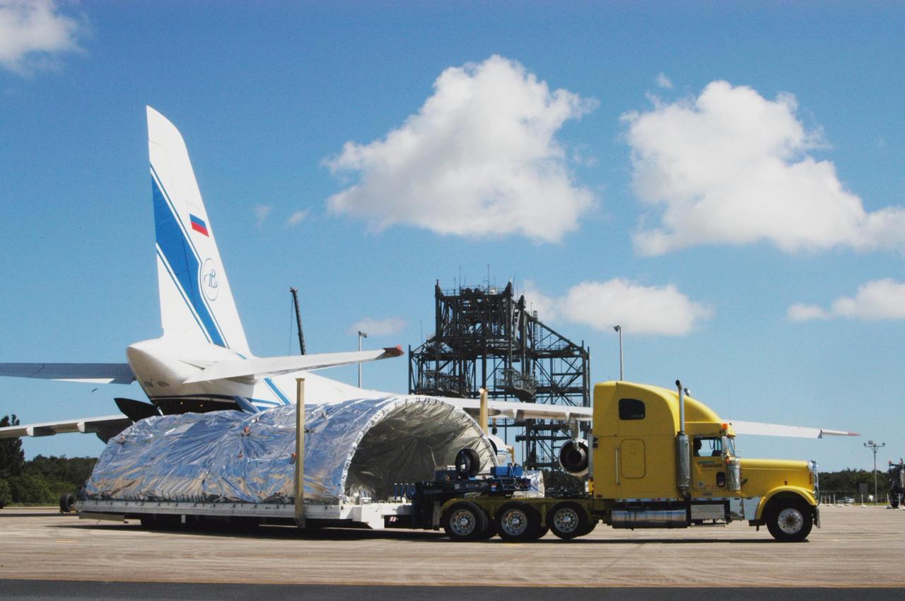 KENNEDY SPACE CENTER, FLA. - On the Shuttle Landing Facility at NASA Kennedy Space Center, one of the Atlas V fairing halves for the New Horizons spacecraft is moved away from the Russian cargo plane that delivered it. Behind the truck is the mate/demate device at the landing facility. The fairing halves will be transported to Astrotech Space Operations in Titusville. The fairing later will be placed around the New Horizons spacecraft in the Payload Hazardous Service Facility. A fairing protects a spacecraft during launch and flight through the atmosphere. Once in space, it is jettisoned. The Lockheed Martin Atlas V is the launch vehicle for the New Horizons spacecraft, which is designed to make the first reconnaissance of Pluto and Charon - a "double planet" and the last planet in our solar system to be visited by spacecraft. The mission will then visit one or more objects in the Kuiper Belt region beyond Neptune. New Horizons is scheduled to launch in January 2006, swing past Jupiter for a gravity boost and scientific studies in February or March 2007, and reach Pluto and its moon, Charon, in July 2015.