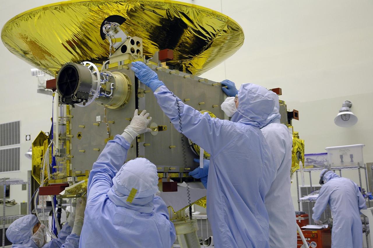 KENNEDY SPACE CENTER, FLA. - At NASA Kennedy Space Center’s Payload Hazardous Servicing Facility, technicians from the Applied Physics Laboratory install another panel on the New Horizons spacecraft. A series of interconnecting panels will enclose the spacecraft beneath the antenna to maintain safe operating temperatures in space. New Horizons will make the first reconnaissance of Pluto and its moon, Charon - a "double planet" and the last planet in our solar system to be visited by spacecraft. As it approaches Pluto, the spacecraft will look for ultraviolet emission from Pluto's atmosphere and make the best global maps of Pluto and Charon in green, blue, red and a special wavelength that is sensitive to methane frost on the surface. It will also take spectral maps in the near infrared, telling the science team about Pluto's and Charon's surface compositions and locations and temperatures of these materials. When the spacecraft is closest to Pluto or its moon, it will take close-up pictures in both visible and near-infrared wavelengths. The mission will then visit one or more objects in the Kuiper Belt region beyond Neptune. New Horizons is scheduled to launch in January 2006, swing past Jupiter for a gravity boost and scientific studies in February or March 2007, and reach Pluto and Charon in July 2015.