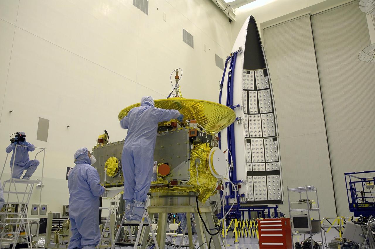 KENNEDY SPACE CENTER, FLA. - At NASA Kennedy Space Center’s Payload Hazardous Servicing Facility, technicians from the Applied Physics Laboratory install another panel on the New Horizons spacecraft. A series of interconnecting panels will enclose the spacecraft beneath the antenna to maintain safe operating temperatures in space. New Horizons will make the first reconnaissance of Pluto and its moon, Charon - a "double planet" and the last planet in our solar system to be visited by spacecraft. As it approaches Pluto, the spacecraft will look for ultraviolet emission from Pluto's atmosphere and make the best global maps of Pluto and Charon in green, blue, red and a special wavelength that is sensitive to methane frost on the surface. It will also take spectral maps in the near infrared, telling the science team about Pluto's and Charon's surface compositions and locations and temperatures of these materials. When the spacecraft is closest to Pluto or its moon, it will take close-up pictures in both visible and near-infrared wavelengths. The mission will then visit one or more objects in the Kuiper Belt region beyond Neptune. New Horizons is scheduled to launch in January 2006, swing past Jupiter for a gravity boost and scientific studies in February or March 2007, and reach Pluto and Charon in July 2015.