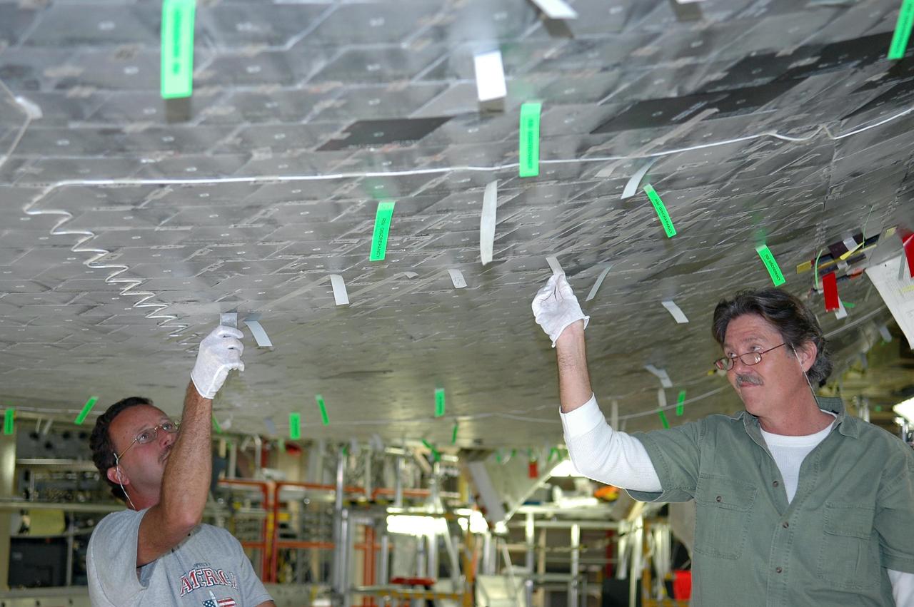 KENNEDY SPACE CENTER, FLA. -   In NASA’s Orbiter Processing Facility Bay 3, United Space Alliance technicians Gene Peavler (left) and Richard McGehee (right) are on a stand removing gap filler and inspecting tile repair on Discovery’s underside. Discovery processing is under way for the second return to flight test mission, STS-121.