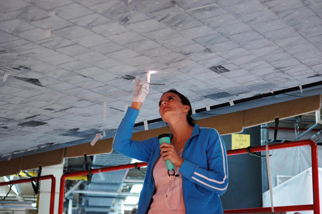 KENNEDY SPACE CENTER, FLA. - In NASA’s Orbiter Processing Facility Bay 3, United Space Alliance technician Erin Schlichenmaier inspects previous tile repair on Discovery’s underside. Discovery processing is under way for the second return to flight test mission, STS-121.