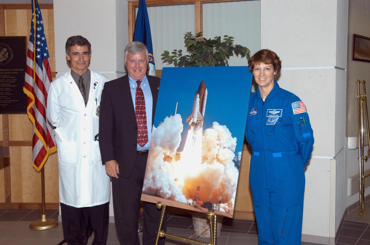 KENNEDY SPACE CENTER, FLA. -   At the V.A. Outpatient Clinic in Viera, Fla., Center Director Jim Kennedy (center) and STS-114 Commander Eileen Collins (right) stand next to the space shuttle Discovery launch photo presented to Dr. Thomas Howard (far left) as part of the dedication of a hospital wing in honor of space shuttle Discovery, to be known as the Discovery wing. Howard is chief medical officer of the clinic. Collins and her crew have returned to Florida especially for a celebration in the KSC Visitor Complex of the successful return to flight mission that launched July 26 of this year.