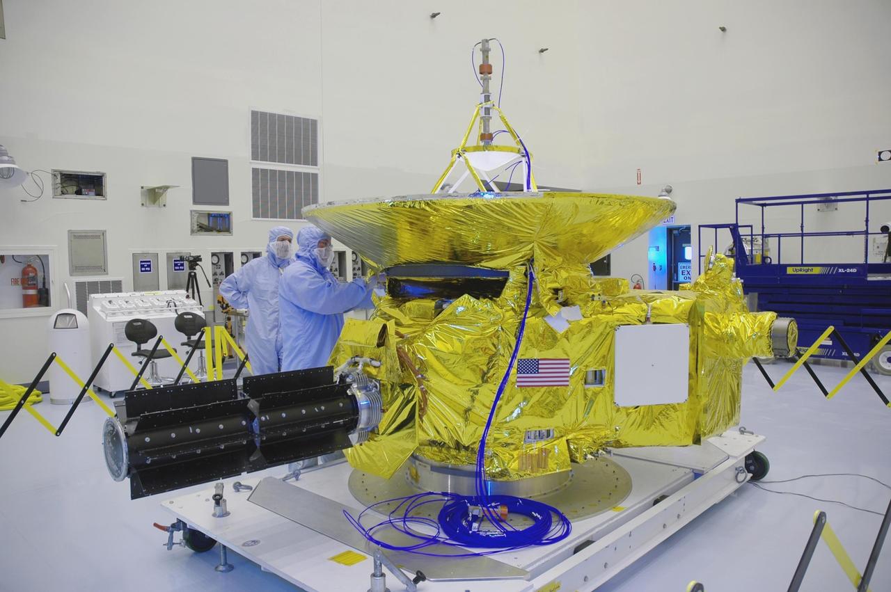 KENNEDY SPACE CENTER, FLA. - In the clean room at KSC’s Payload Hazardous Servicing Facility, technicians prepare the New Horizons spacecraft for a media event. Photographers and reporters will be able to photograph the New Horizons spacecraft and talk with project management and test team members from NASA and the Johns Hopkins University Applied Physics Laboratory. Seen behind the spacecraft is one half of the fairing that will enclose it for launch, scheduled for January 2006. Carrying seven scientific instruments, the compact 1,060-pound New Horizons probe will characterize the global geology and geomorphology of Pluto and its moon Charon, map their surface compositions and temperatures, and examine Pluto's complex atmosphere. After that, flybys of Kuiper Belt objects from even farther in the solar system may be undertaken in an extended mission. New Horizons is the first mission in NASA's New Frontiers program of medium-class planetary missions. The spacecraft, designed for NASA by the Johns Hopkins University Applied Physics Laboratory in Laurel, Md., will fly by Pluto and Charon as early as summer 2015.