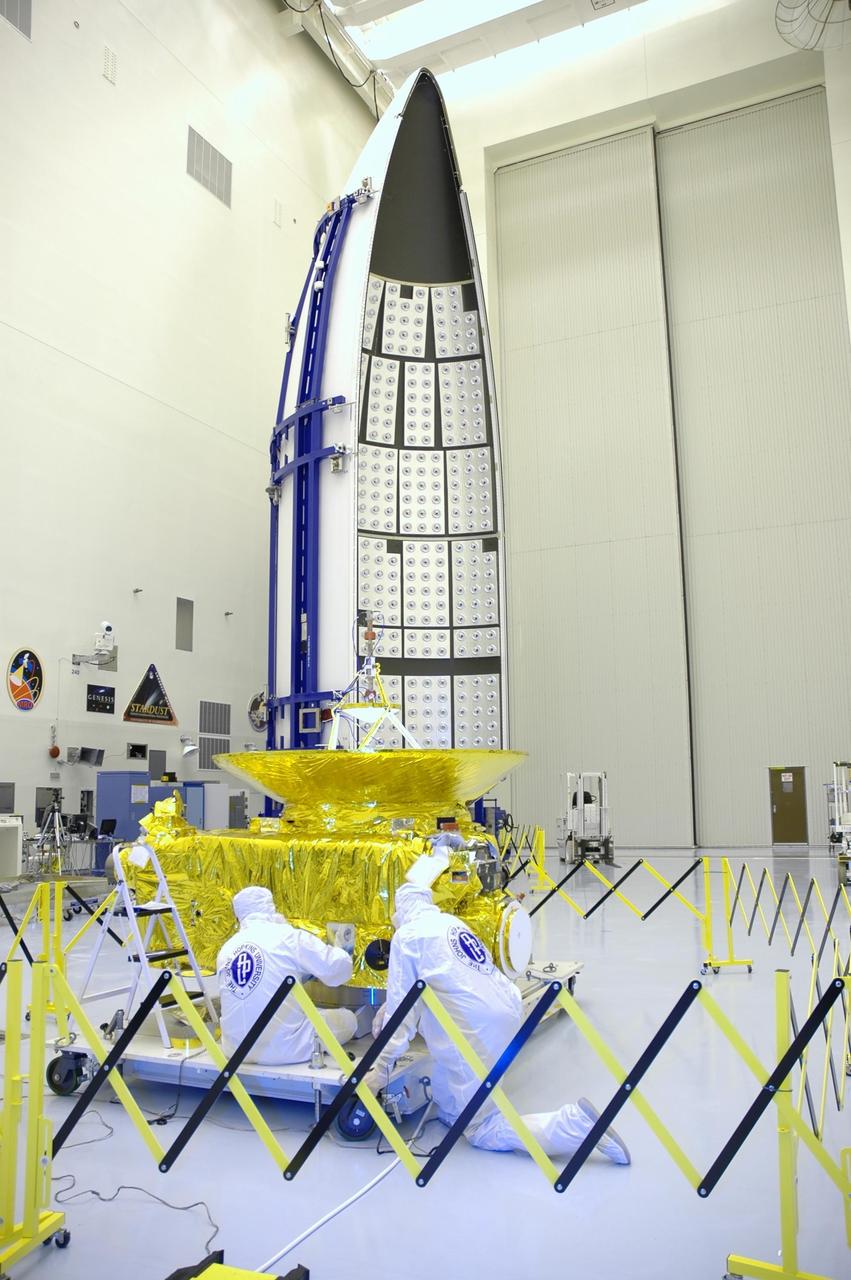 KENNEDY SPACE CENTER, FLA. - In the clean room at KSC’s Payload Hazardous Servicing Facility, technicians prepare the New Horizons spacecraft for a media event. Photographers and reporters will be able to photograph the New Horizons spacecraft and talk with project management and test team members from NASA and the Johns Hopkins University Applied Physics Laboratory. Seen behind the spacecraft is one half of the fairing that will enclose it for launch, scheduled for January 2006. Carrying seven scientific instruments, the compact 1,060-pound New Horizons probe will characterize the global geology and geomorphology of Pluto and its moon Charon, map their surface compositions and temperatures, and examine Pluto's complex atmosphere. After that, flybys of Kuiper Belt objects from even farther in the solar system may be undertaken in an extended mission. New Horizons is the first mission in NASA's New Frontiers program of medium-class planetary missions. The spacecraft, designed for NASA by the Johns Hopkins University Applied Physics Laboratory in Laurel, Md., will fly by Pluto and Charon as early as summer 2015.