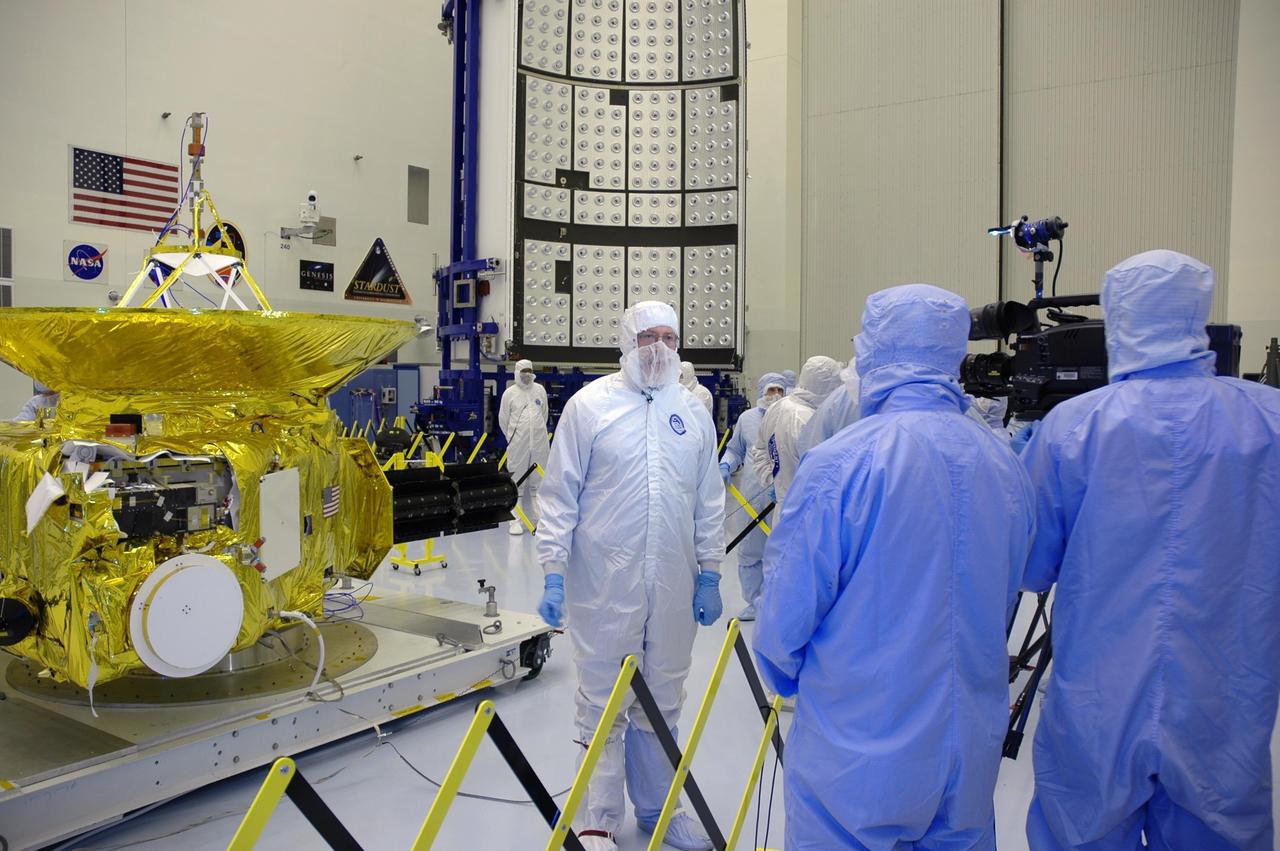 KENNEDY SPACE CENTER, FLA. - In the clean room at KSC’s Payload Hazardous Servicing Facility, the media (also dressed in clean room suits) learn about NASA’s New Horizons spacecraft (at left) from New Horizons Mission Systems Engineer David Kusnierkiewicz, in the center. Behind Kusnierkiewicz is one half of the fairing that will enclose the spacecraft for launch, scheduled for January 2006. The media event brought photographers and reporters to the site to talk with project management and test team members from NASA and the Johns Hopkins University Applied Physics Laboratory. Carrying seven scientific instruments, the compact 1,060-pound New Horizons probe will characterize the global geology and geomorphology of Pluto and its moon Charon, map their surface compositions and temperatures, and examine Pluto's complex atmosphere. After that, flybys of Kuiper Belt objects from even farther in the solar system may be undertaken in an extended mission. New Horizons is the first mission in NASA's New Frontiers program of medium-class planetary missions. The spacecraft, designed for NASA by the Johns Hopkins University Applied Physics Laboratory in Laurel, Md., will fly by Pluto and Charon as early as summer 2015.