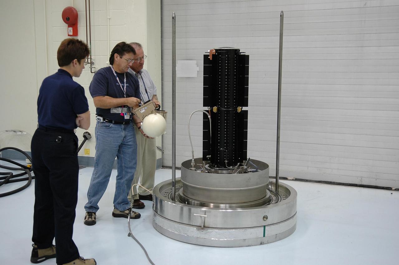 KENNEDY SPACE CENTER, FLA. - Inside the RTG facility at Kennedy Space Center, Amy Powell, Ennis Shelton and Ed Provost check the radioisotope thermoelectric generator (RTG) after removal of the outside container. The RTG is the baseline power supply for the NASA’s New Horizons spacecraft, scheduled to launch in January 2006 on a journey to Pluto and its moon, Charon. As it approaches Pluto, the spacecraft will look for ultraviolet emission from Pluto's atmosphere and make the best global maps of Pluto and Charon in green, blue, red and a special wavelength that is sensitive to methane frost on the surface. It will also take spectral maps in the near infrared, telling the science team about Pluto's and Charon's surface compositions and locations and temperatures of these materials. When the spacecraft is closest to Pluto or its moon, it will take close-up pictures in both visible and near-infrared wavelengths. It is expected to reach Pluto in July 2015.