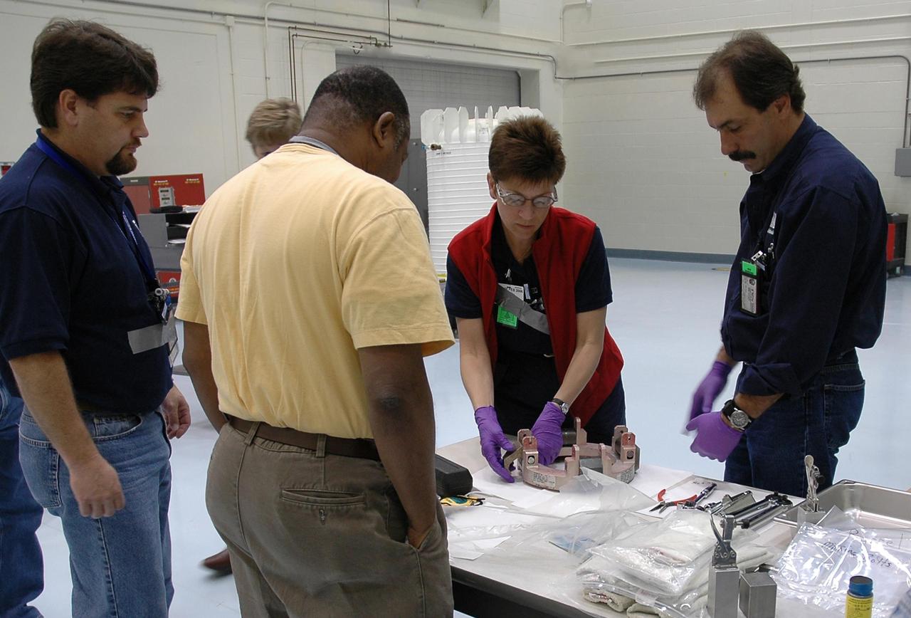 KENNEDY SPACE CENTER, FLA. - In the RTG Facility at Kennedy Space Center, Rhett Rovig, Mervin Smith, Amy Powell and June Wojciechowski inspect a clamping ring that will be installed on the radioisotope thermoelectric generator (RTG). The RTG is the baseline power supply for the NASA’s New Horizons spacecraft, scheduled to launch in January 2006 on a journey to Pluto and its moon, Charon. As it approaches Pluto, the spacecraft will look for ultraviolet emission from Pluto's atmosphere and make the best global maps of Pluto and Charon in green, blue, red and a special wavelength that is sensitive to methane frost on the surface. It will also take spectral maps in the near infrared, telling the science team about Pluto's and Charon's surface compositions and locations and temperatures of these materials. When the spacecraft is closest to Pluto or its moon, it will take close-up pictures in both visible and near-infrared wavelengths. It is expected to reach Pluto in July 2015.