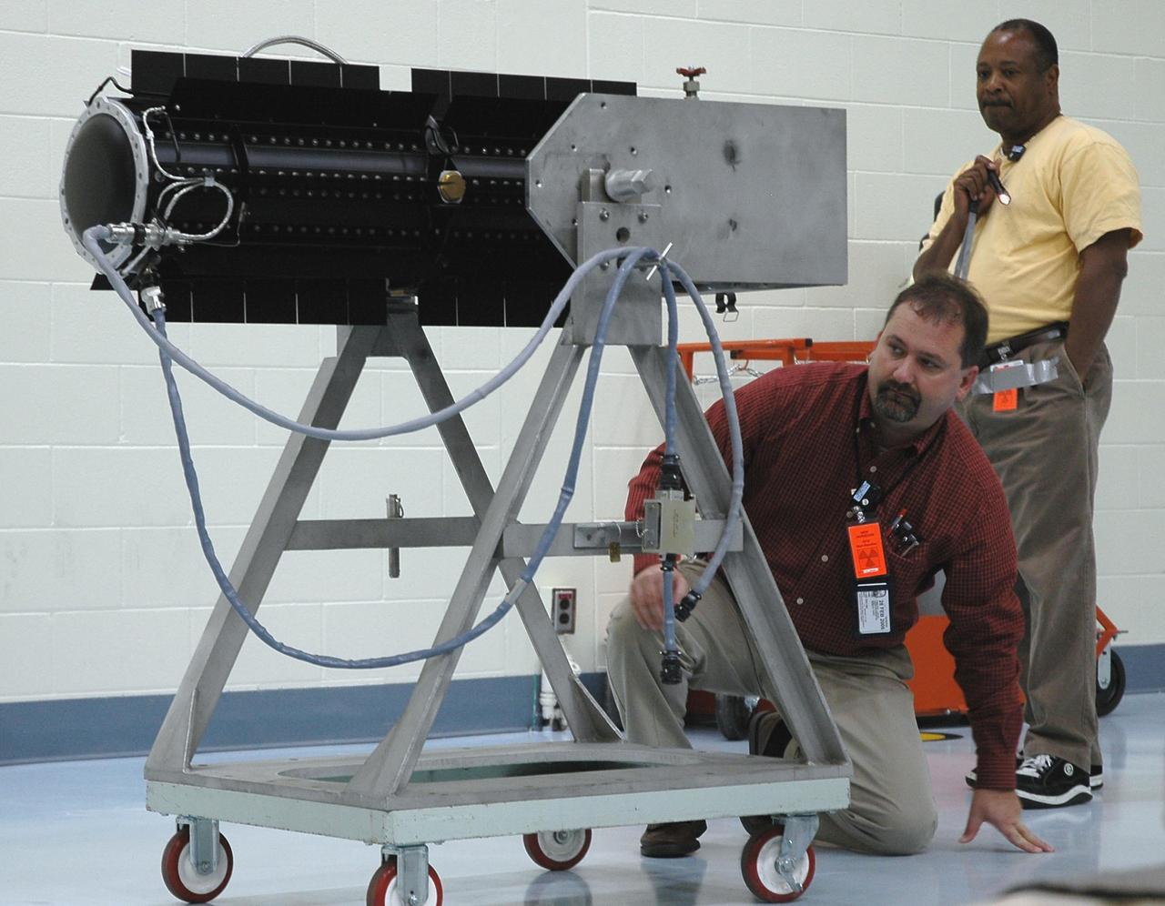 KENNEDY SPACE CENTER, FLA. - In the RTG Facility at Kennedy Space Center, Tim Hoyle and Mervin Smith check the cable on the radioisotope thermoelectric generator (RTG). The RTG is the baseline power supply for the NASA’s New Horizons spacecraft, scheduled to launch in January 2006 on a journey to Pluto and its moon, Charon. As it approaches Pluto, the spacecraft will look for ultraviolet emission from Pluto's atmosphere and make the best global maps of Pluto and Charon in green, blue, red and a special wavelength that is sensitive to methane frost on the surface. It will also take spectral maps in the near infrared, telling the science team about Pluto's and Charon's surface compositions and locations and temperatures of these materials. When the spacecraft is closest to Pluto or its moon, it will take close-up pictures in both visible and near-infrared wavelengths. It is expected to reach Pluto in July 2015.