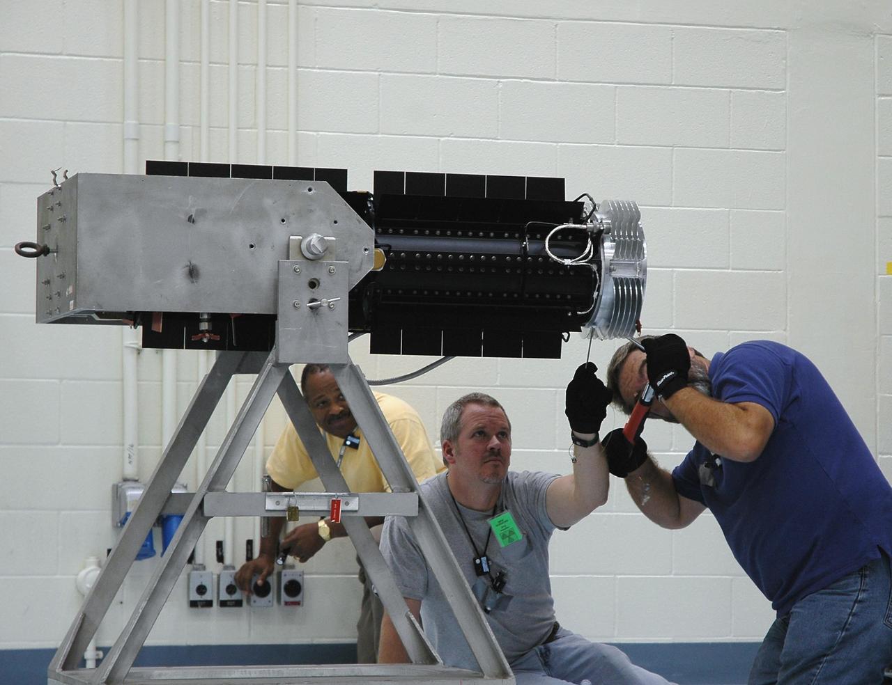 KENNEDY SPACE CENTER, FLA. - In the RTG Facility at Kennedy Space Center, Mervin Smith watches as technicians install a flight adapter on the radioisotope thermoelectric generator (RTG). The RTG is the baseline power supply for the NASA’s New Horizons spacecraft, scheduled to launch in January 2006 on a journey to Pluto and its moon, Charon. As it approaches Pluto, the spacecraft will look for ultraviolet emission from Pluto's atmosphere and make the best global maps of Pluto and Charon in green, blue, red and a special wavelength that is sensitive to methane frost on the surface. It will also take spectral maps in the near infrared, telling the science team about Pluto's and Charon's surface compositions and locations and temperatures of these materials. When the spacecraft is closest to Pluto or its moon, it will take close-up pictures in both visible and near-infrared wavelengths. It is expected to reach Pluto in July 2015.