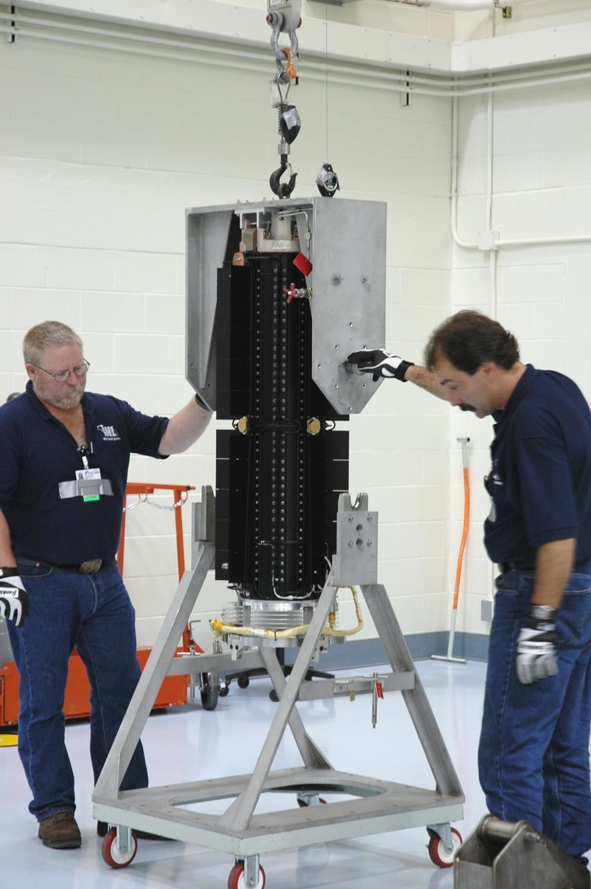 KENNEDY SPACE CENTER, FLA. - In the RTG Facility at Kennedy Space Center, Dan Brunson and Jim Wojciechowski carefully lower the radioisotope thermoelectric generator (RTG) into a t-cart. The RTG is the baseline power supply for the NASA’s New Horizons spacecraft, scheduled to launch in January 2006 on a journey to Pluto and its moon, Charon. As it approaches Pluto, the spacecraft will look for ultraviolet emission from Pluto's atmosphere and make the best global maps of Pluto and Charon in green, blue, red and a special wavelength that is sensitive to methane frost on the surface. It will also take spectral maps in the near infrared, telling the science team about Pluto's and Charon's surface compositions and locations and temperatures of these materials. When the spacecraft is closest to Pluto or its moon, it will take close-up pictures in both visible and near-infrared wavelengths. It is expected to reach Pluto in July 2015.