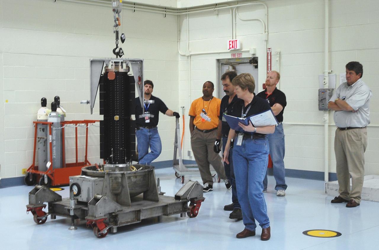 KENNEDY SPACE CENTER, FLA. - In the RTG Facility at Kennedy Space Center, officials check the radioisotope thermoelectric generator (RTG) after being lowered onto a transporter. The RTG is the baseline power supply for the NASA’s New Horizons spacecraft, scheduled to launch in January 2006 on a journey to Pluto and its moon, Charon. As it approaches Pluto, the spacecraft will look for ultraviolet emission from Pluto's atmosphere and make the best global maps of Pluto and Charon in green, blue, red and a special wavelength that is sensitive to methane frost on the surface. It will also take spectral maps in the near infrared, telling the science team about Pluto's and Charon's surface compositions and locations and temperatures of these materials. When the spacecraft is closest to Pluto or its moon, it will take close-up pictures in both visible and near-infrared wavelengths. It is expected to reach Pluto in July 2015.