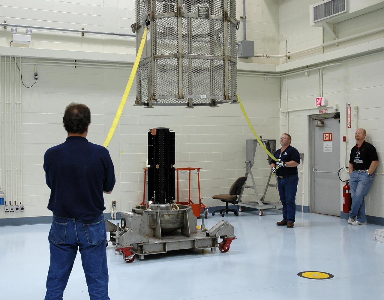KENNEDY SPACE CENTER, FLA. - n the RTG Facility at Kennedy Space Center, Jim Wojciechowski and Dan Brunson move a metal canister toward the radioisotope thermoelectric generator (RTG). The canister will protect the RTG when it is moved. The RTG is the baseline power supply for the NASA’s New Horizons spacecraft, scheduled to launch in January 2006 on a journey to Pluto and its moon, Charon. As it approaches Pluto, the spacecraft will look for ultraviolet emission from Pluto's atmosphere and make the best global maps of Pluto and Charon in green, blue, red and a special wavelength that is sensitive to methane frost on the surface. It will also take spectral maps in the near infrared, telling the science team about Pluto's and Charon's surface compositions and locations and temperatures of these materials. When the spacecraft is closest to Pluto or its moon, it will take close-up pictures in both visible and near-infrared wavelengths. It is expected to reach Pluto in July 2015.
