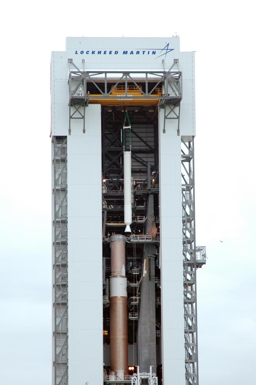 KENNEDY SPACE CENTER, FLA. - In the Vertical Integration Facility on Launch Complex 41 at Cape Canaveral Air Force Station in Florida, a solid rocket booster is being lowered into position on the Atlas V rocket at left. The Atlas V is the launch vehicle for NASA’s New Horizons spacecraft, scheduled to launch in January 2006 on a journey to Pluto and its moon, Charon.