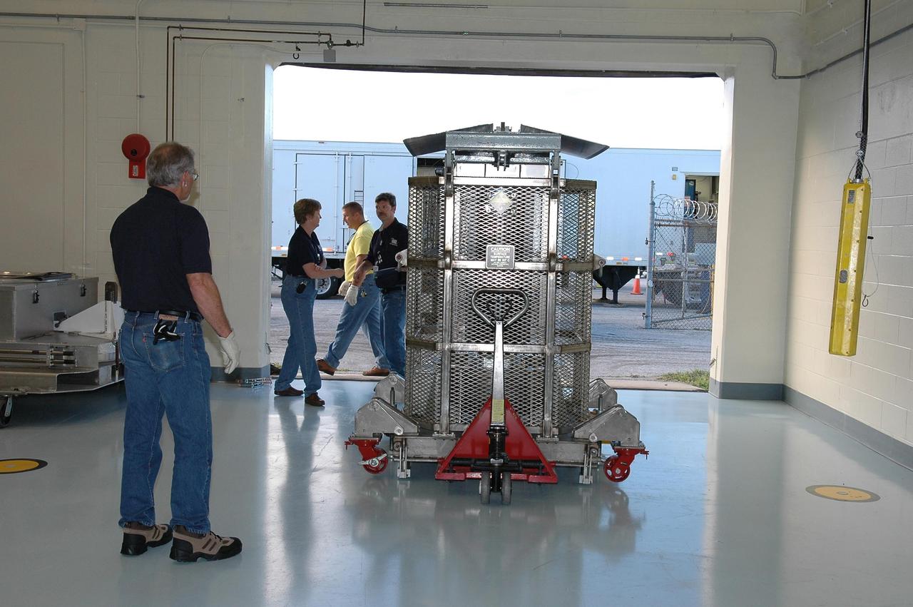 KENNEDY SPACE CENTER, FLA. - In NASA Kennedy Space Center’s Payload Hazardous Servicing Facility, Boeing workers garbed in clean room suits move the protective cover of the transportation canister away from the third stage, or upper stage, for the New Horizons spacecraft, in the background. The third stage is a Boeing STAR 48 solid-propellant kick motor.  The launch vehicle for New Horizons is the Atlas V rocket, scheduled to launch from Cape Canaveral Air Force Station, Fla., during a 35-day window that opens Jan. 11, and fly through the Pluto system as early as summer 2015.