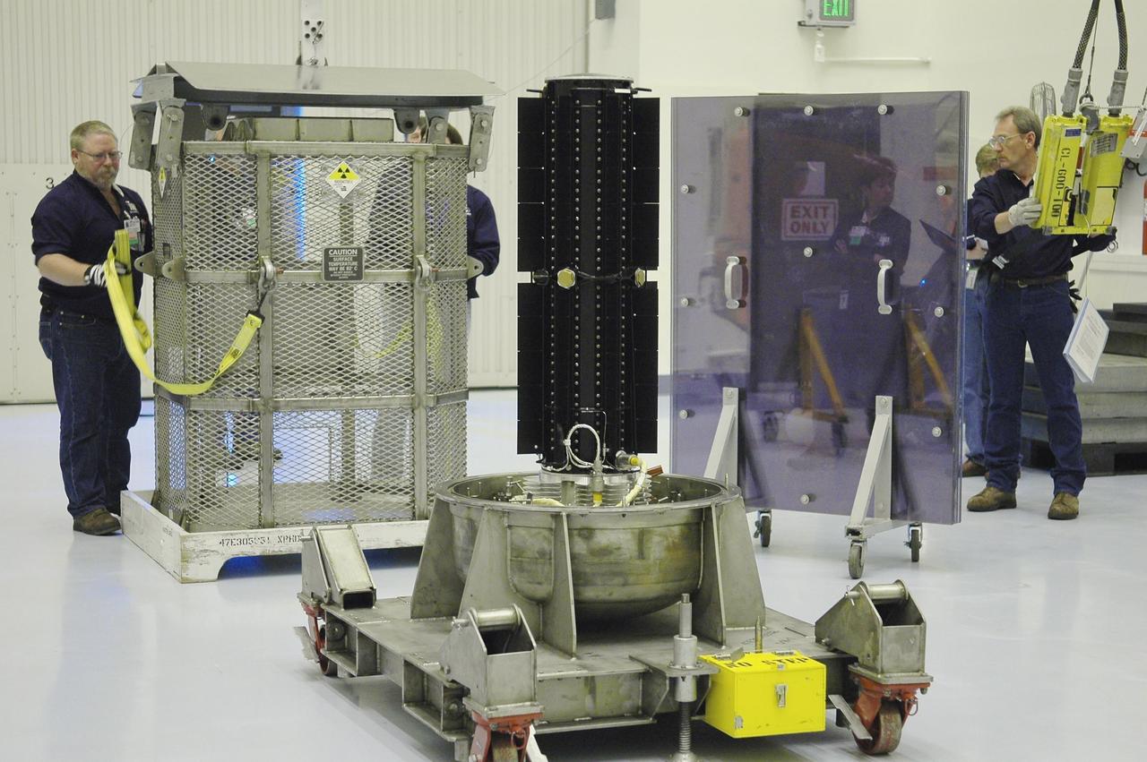 KENNEDY SPACE CENTER, FLA. - In NASA Kennedy Space Center’s Payload Hazardous Servicing Facility, the metal canister is secured at left. In the center is the radioisotope thermoelectric generator (RTG) that will be installed in the New Horizons spacecraft for a fit check. The RTG is the baseline power supply for New Horizons, scheduled to launch in January 2006 on a journey to Pluto and its moon, Charon. It is expected to reach Pluto in July 2015.