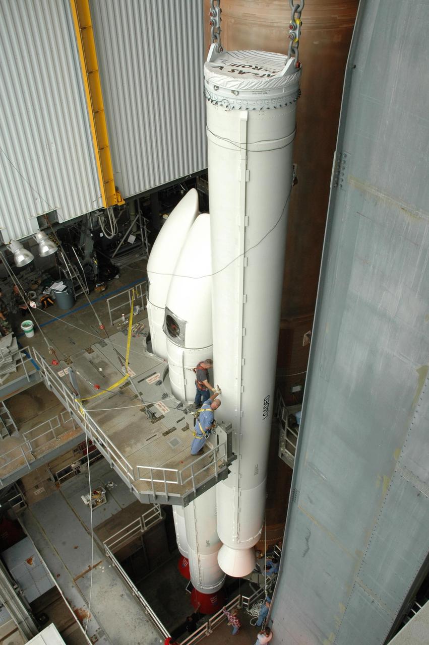 KENNEDY SPACE CENTER, FLA. - In the Vertical Integration Facility on Launch Complex 41 at Cape Canaveral Air Force Station in Florida, workers maneuver the fifth and final solid rocket booster into place for mating to the Lockheed Martin Atlas V rocket. Two of the other four rockets are seen at left. The Atlas V is the launch vehicle for the Pluto-bound New Horizons spacecraft that will make the first reconnaissance of Pluto and its moon, Charon - a "double planet" and the last planet in our solar system to be visited by spacecraft. As it approaches Pluto, the spacecraft will look for ultraviolet emission from Pluto's atmosphere and make the best global maps of Pluto and Charon in green, blue, red and a special wavelength that is sensitive to methane frost on the surface. It will also take spectral maps in the near infrared, telling the science team about Pluto's and Charon’s surface compositions and locations and temperatures of these materials. When the spacecraft is closest to Pluto or its moon, it will take close-up pictures in both visible and near-infrared wavelengths. The mission will then visit one or more objects in the Kuiper Belt region beyond Neptune. New Horizons is scheduled to launch in January 2006, swing past Jupiter for a gravity boost and scientific studies in February or March 2007, and reach Pluto and Charon in July 2015.