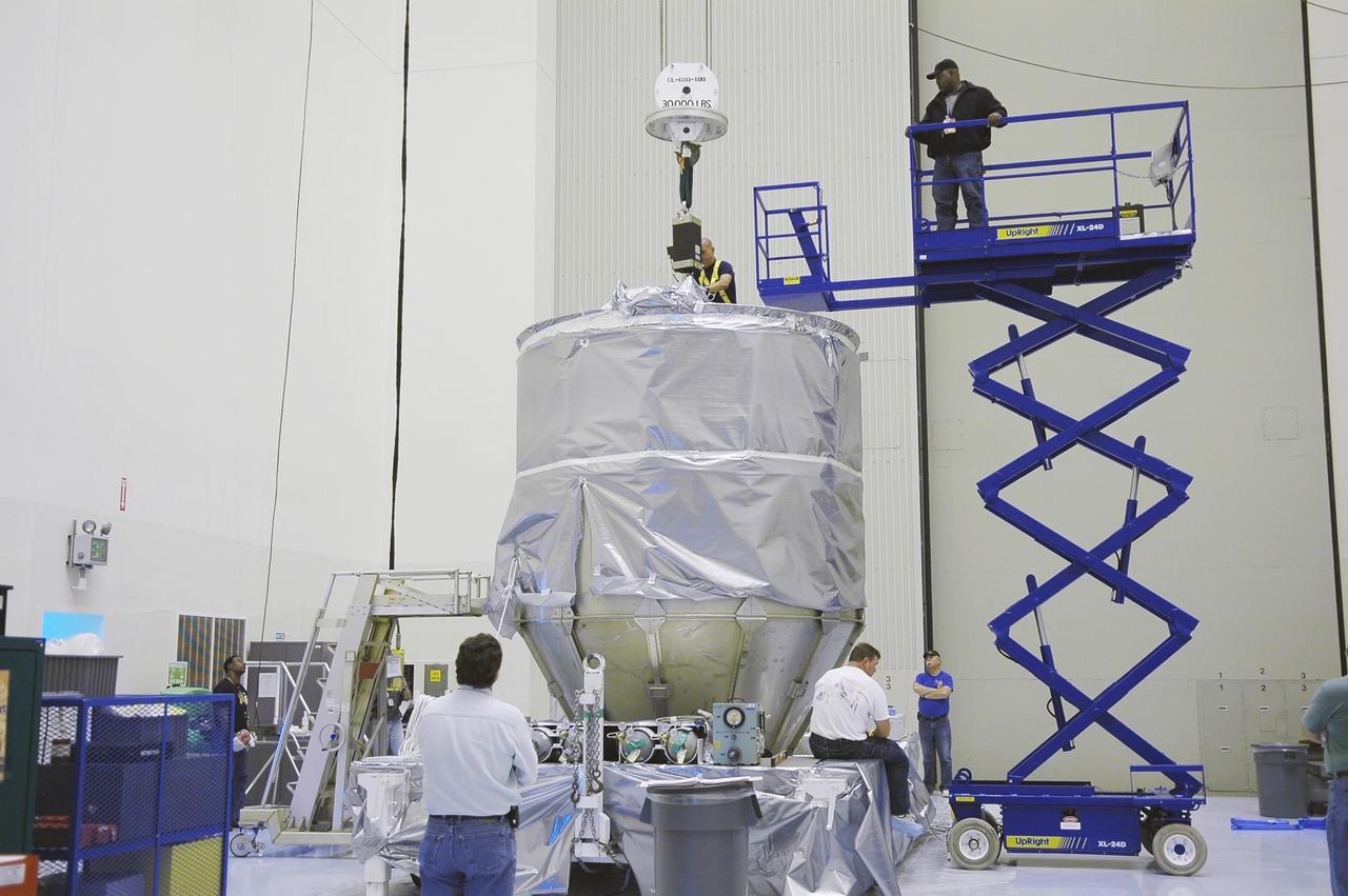 KENNEDY SPACE CENTER, FLA. -     In NASA Kennedy Space Center’s Payload Hazardous Servicing Facility, Boeing workers attach a crane to the top of the cover surrounding the third stage, or upper stage, for the New Horizons spacecraft. The third stage is a Boeing STAR 48 solid-propellant kick motor.  The launch vehicle for New Horizons is the Atlas V rocket, scheduled to launch from Cape Canaveral Air Force Station, Fla., during a 35-day window that opens Jan. 11, and fly through the Pluto system as early as summer 2015.