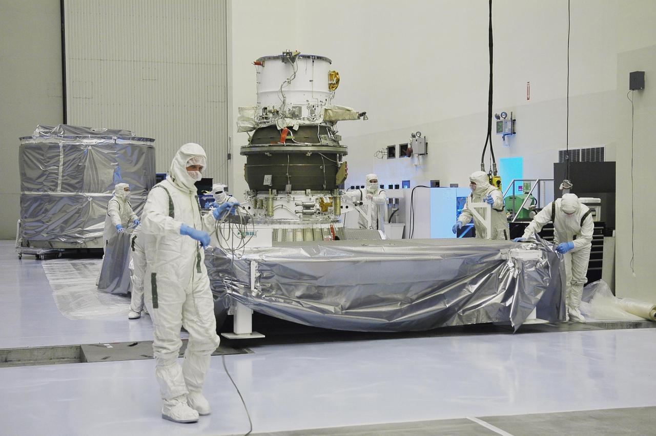 KENNEDY SPACE CENTER, FLA. -   In NASA Kennedy Space Center’s Payload Hazardous Servicing Facility, Boeing workers garbed in clean room suits move the protective cover of the transportation canister away from the third stage, or upper stage, for the New Horizons spacecraft, in the background.  The third stage is a Boeing STAR 48 solid-propellant kick motor.  The launch vehicle for New Horizons is the Atlas V rocket, scheduled to launch from Cape Canaveral Air Force Station, Fla., during a 35-day window that opens Jan. 11, and fly through the Pluto system as early as summer 2015.