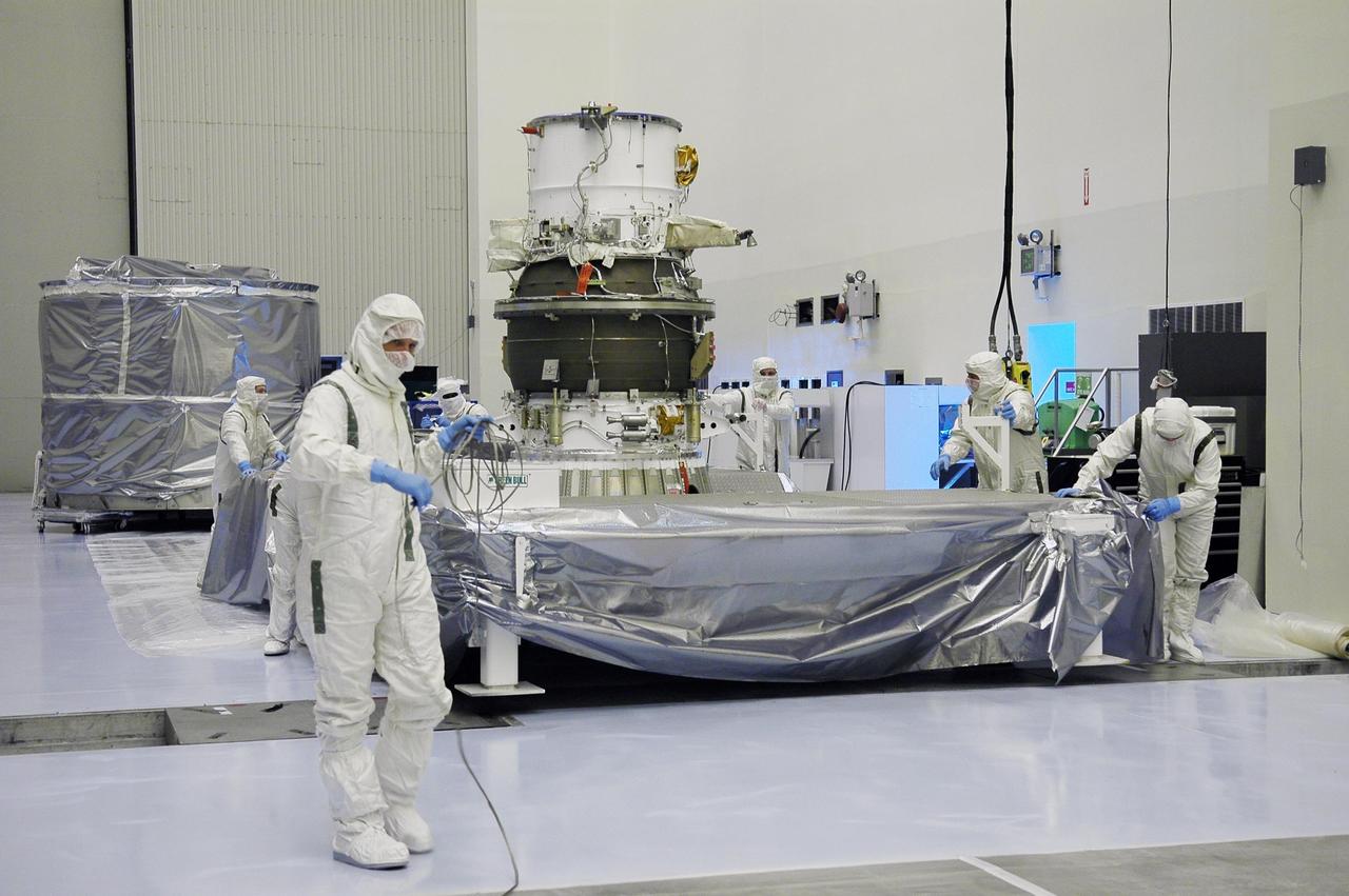 KENNEDY SPACE CENTER, FLA. -   In NASA Kennedy Space Center’s Payload Hazardous Servicing Facility, Boeing workers garbed in clean room suits move the protective cover of the transportation canister away from the third stage, or upper stage, for the New Horizons spacecraft, in the background.  The third stage is a Boeing STAR 48 solid-propellant kick motor.  The launch vehicle for New Horizons is the Atlas V rocket, scheduled to launch from Cape Canaveral Air Force Station, Fla., during a 35-day window that opens Jan. 11, and fly through the Pluto system as early as summer 2015.